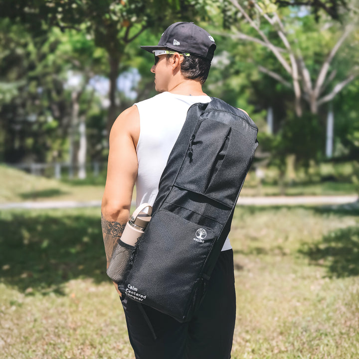 Man carrying a warrior2 black sling yoga bag outdoors in a park