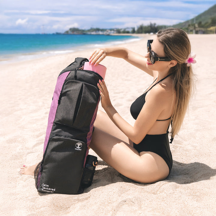 Woman sitting on a beach with a warrior2 yoga bag in grey and charkra purple colors sunshine white sand