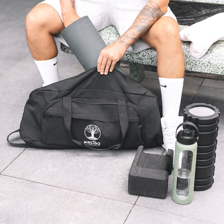 Person with gym equipment including a warrior2 black duffel bag, water bottle, and weights on a tiled floor.
