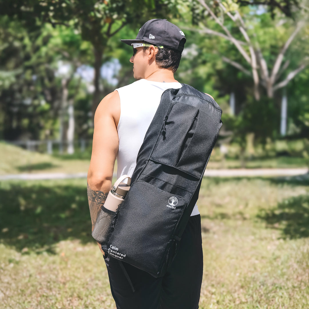 Man carrying a warrior2 black sling yoga bag outdoors in a park