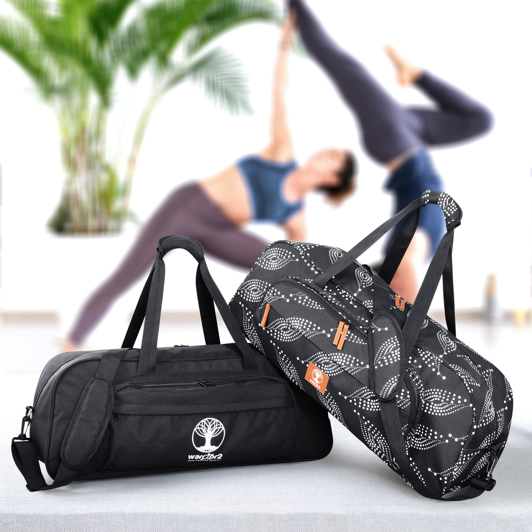 Two warrior2 yoga gym bags, one black and one with a black and white paisley pattern, in the foreground with blurred women practicing yoga in the background