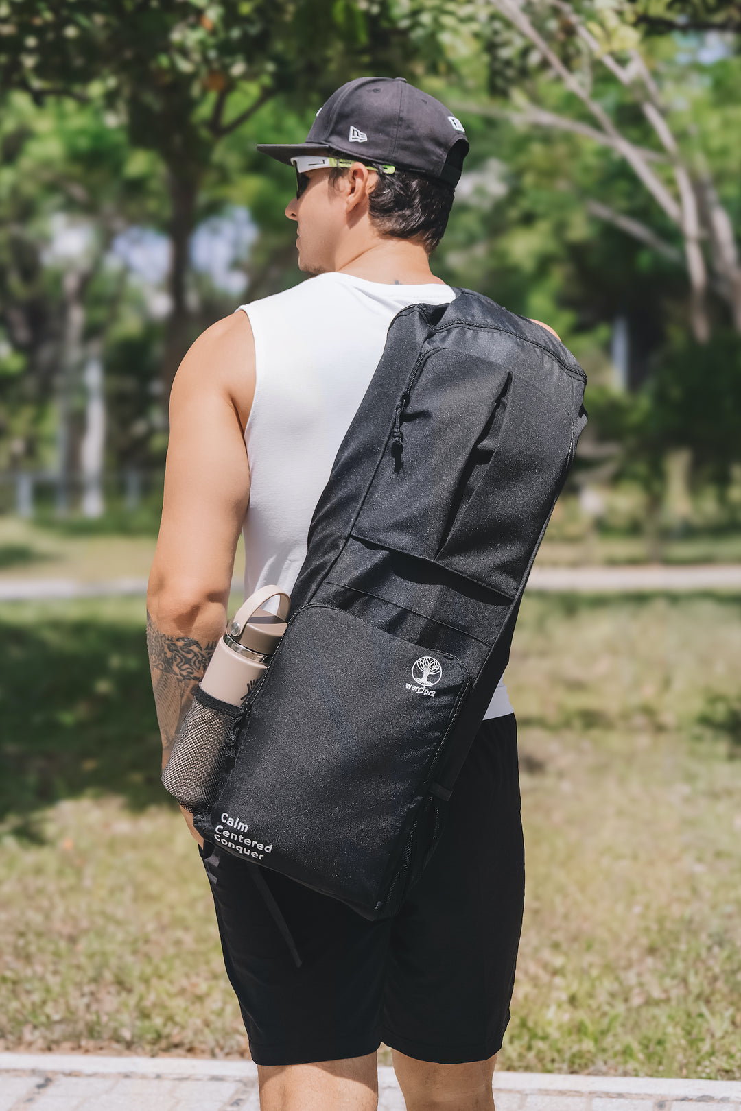 Person carrying a black bag outdoors with greenery in the background