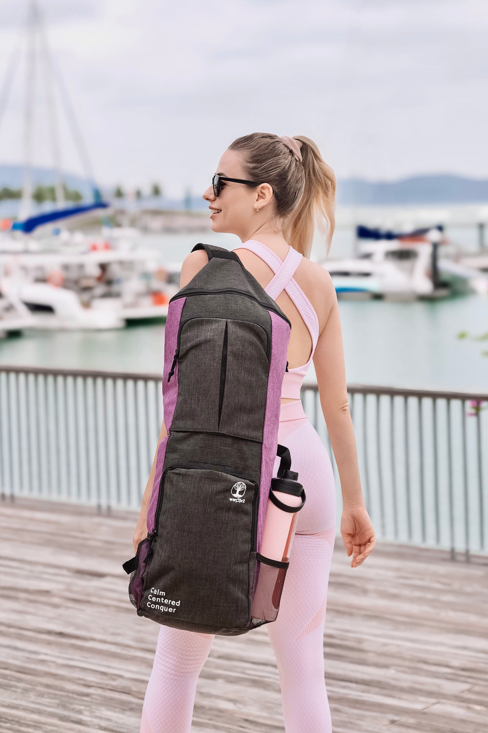 girl in pink active wear carrying warrior2 yoga bag smiling by the ocean