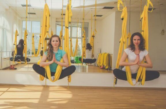 two women yellow hammocks aerial yoga studio