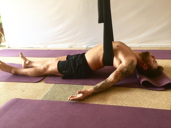 man doing aerial yoga lying on floor with arched chest