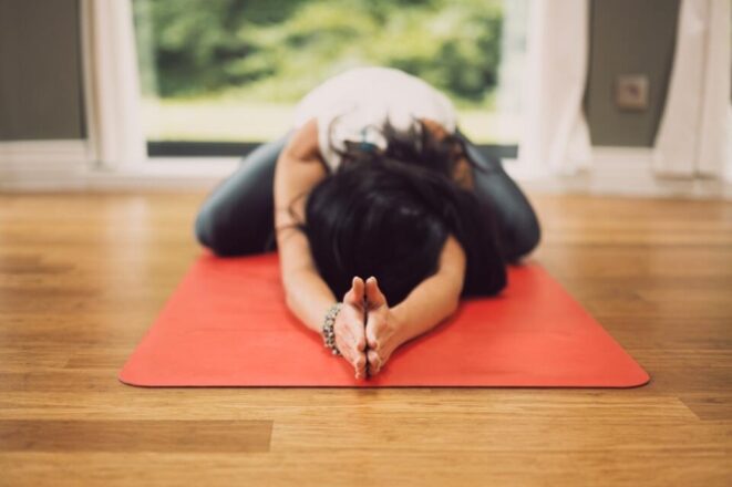 woman yoga child pose on red yoga mat wooden floor