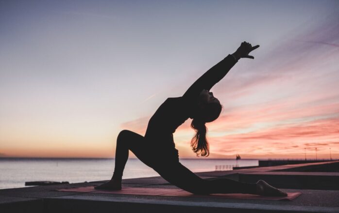 woman doing yoga sunset dark next to water