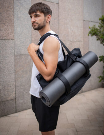 man in white singlet on the street carrying warrior2 yoga gym bag